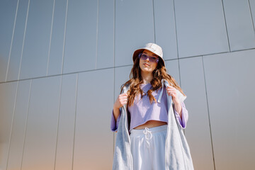 Young hip hop girl in oversize outfit wearing dancing into music minimalistic urban background. 
