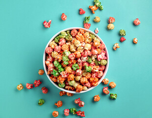 Bowl of sweet colorful popcorn on blue background, top view