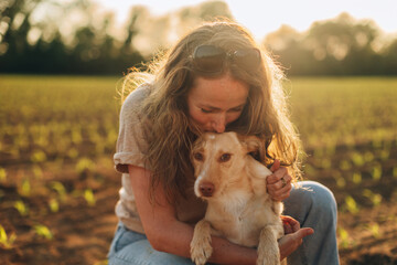 happy woman in love with her dog - lady kiss her pet outdoors in sunset