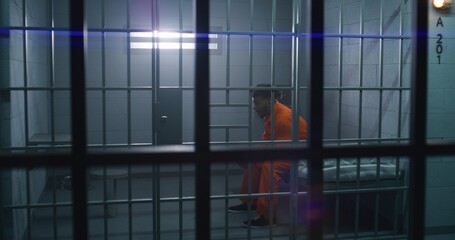 Man in orange uniform gives food from serving trolley to prisoner in jail cell. Depressed criminal...