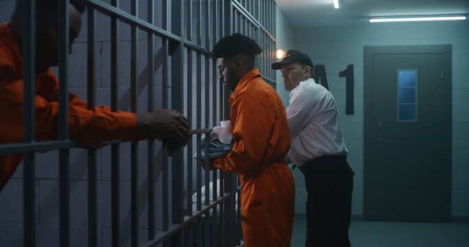 Warden brings new prisoner in jail cell and takes off his handcuffs. African American criminals serve imprisonment term in correctional facility or detention center. Guilty murderers in prison cells.