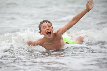 Happy boy playing with the sea wave, enjoying the sea. The child bathes, sunbathes and rests. Summer holidays.