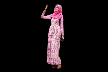 Portrait of smiling young Muslim woman wearing pink hijab with red rose flower motif dress waving right arm up gesture and left hand holding phone. Happy and cheerful expression.