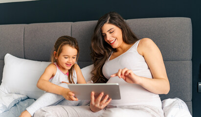 Mom and daughter sitting on a bed and bounding before new baby arrives, watching cartoons on tablet...