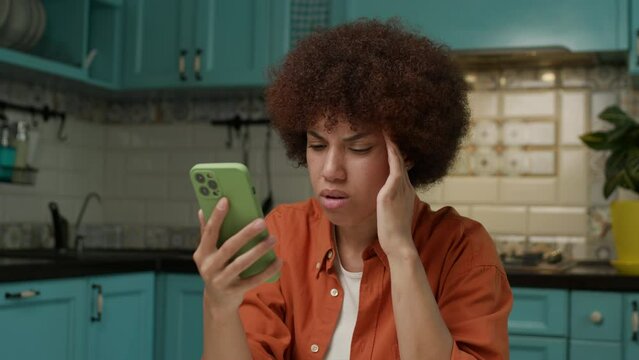 Black Woman Reading Bad News on Cell Phone Sitting at Home Alone. Upset female using smartphone.