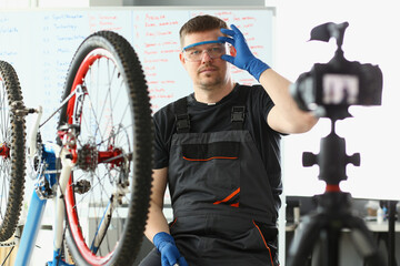 Smiling vlogger in glasses with bicycle remote repair. Blogger talks in blog about bicycles