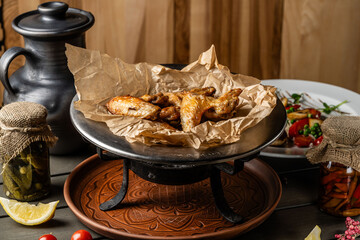 Turkish cuisine, fried chicken wings, lie on a special plate with coals on a dark background in a restaurant.