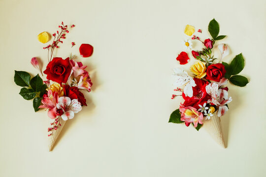 Two fancy improvised flower ice creams of red roses and alstroemeria left and right photo, empty space in the center, flat lay. Bright farm garden flowers in waffle ice cream cone on beige background.