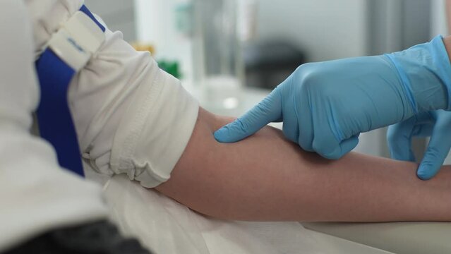 Closeup hands of unrecognizable female nurse in protective gloves locating and searching for veins for injection. Close up of woman doctor taking blood sample from patient at laboratory, slow motion.