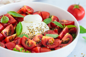Burrata salad with tomatoes and basil in white plate.