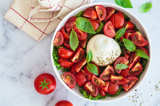 Burrata salad with tomatoes and basil in white plate.
