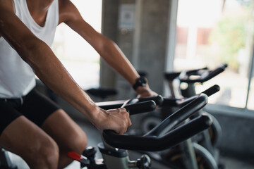 Fototapeta na wymiar Close up hands of asian sportsman exercising on a bicycle in the gym, determination to cardio lose weight, makes her healthy. exercise bike man fitness sport concept.