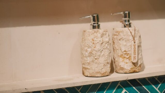 Person hand taking shampoo bottles on a bathroom shelf. Beautiful natural eco style design of shower body wash. luxury life in spa tropical resort. Hygge lifestyle. Shampoo jars in the form of stones.