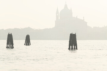 Venetian basilica silhouette backlight with wood moorings in St Mark basin in Venice, Italy