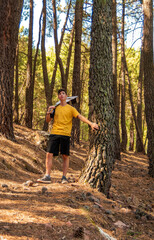 Obraz premium young man in yellow t-shirt playing a tree in a pine forest with a guitar in his hand