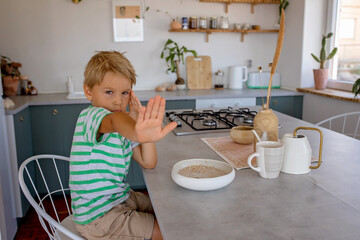 Beautiful blond child, boy, refusing to eat cereal for breakfast at home in the morning