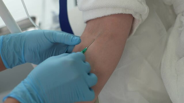 Close-up hands of unrecognizable female nurse in medical gloves inserting IV catheter into woman patient arm. Process of administering drugs intravenously. Shooting in slow motion.