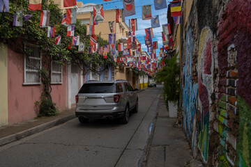 SUV truck driving through a small narrow street decorated with many different countries flags in Cartagena, Colombia.
