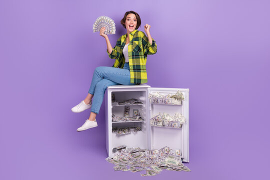 Full body photo of funky young overjoyed woman winnings millions dollars much money fridge banknotes isolated on violet color background