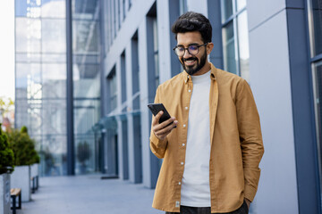 Young successful businessman walking in the city outside office building, hispanic smiling happy...