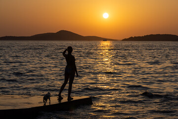 A young woman is standing on a pier, looking at the sunset on the Adriatic Sea in Croatia.
