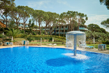 Relaxation swimming pool in a leisure camp. Empty Swimming pool with waterfall jet. Pool side on summer sunny day. Seaside vacation and hotel resort concept. Reflection in blue clean sea water pool