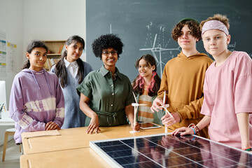 Portrait of teacher and students smiling at camera while standing in the classroom