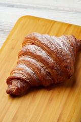 Freshly baked croissant with powdered sugar on wooden board