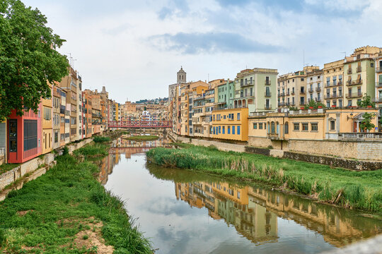 Colorful yellow and orange houses and bridge Pont de Sant Agusti reflected in water river Onyar, in Girona, Catalonia, Spain. Church of Sant Feliu and Saint Mary Cathedral at background. BRIDGE in the