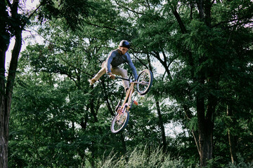 Summer activity. Young sportive man riding bmx bike in forest, doing dangerous and difficult...
