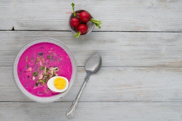 Chłodnik, Šaltibarščiai is traditional lithuanian, polish beet soup. Cold summer soup of beetroot, kefir, cucumbers, eggs, dill and radish in a bowl on a wood table. Summer Healthy food. Top view