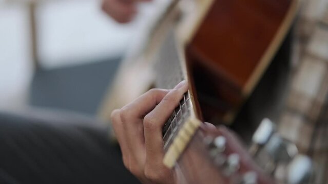 Close up of hand playing acoustic guitar on couch. Music, entertainment and leisure activity concept