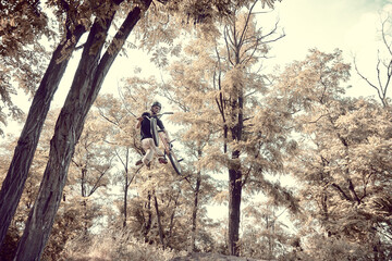 Naklejka premium Dangerous activity. Young man, professional rider training in forest, doing tricks with bmx bike. Concept of active lifestyle, sport, extreme, dynamics, hobby, freestyle