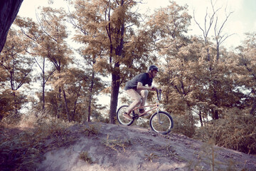 Young man in helmet training outdoors in forest, riding bmx bike, doing tricks. Autumn ride,...
