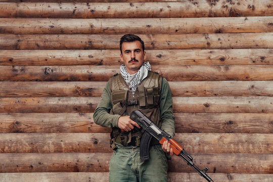 A soldier in uniform with a rifle in his hand is standing in front of a wooden wall. A soldier guards the forest base from the enemy