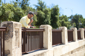 handsome young man with beard and sunglasses is leaning on the railing of a park and looks down. The man is depressed and is going through a bad time in his life. Mental health concept.