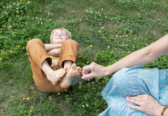 concept of a friendly cheerful family, mom plays with her son lying on the grass, gently tickling...