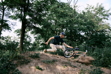 Fototapeta na wymiar Young man in helmet riding bmx bike in forest, doing dangerous tricks and falling down. Difficult training before race. Concept of active lifestyle, sport, extreme, dynamics, hobby, freestyle