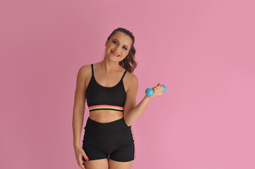 mulher com roupa de treino fitness segurando peso de academia em fundo rosa 