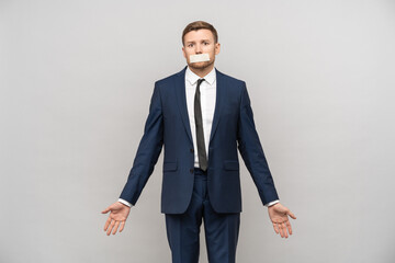 Confused man with mouth sealed in adhesive tape. Sad male shrugging shoulders in despair with close lips in message about free of speech, freedom expression, Human rights, democracy, liberty, equality