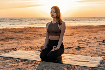 Fototapeta na wymiar Concentration and mental health. Yoga workout at sunset, a young woman slender beautiful body, workout uses a mat on the sand. Zen and meditation.