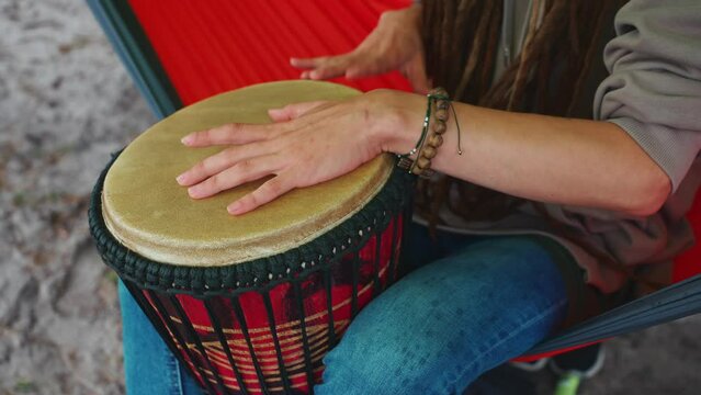 person with dreadlocks play tribal reggae at small African hand drum djembe