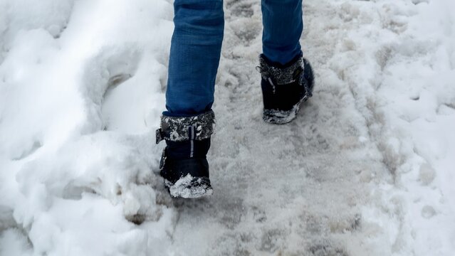 Closeup of boy in snowboots walking over covered snowdrifts and road covered with snow and ice
