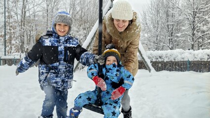 Happy family with two sons playing and riding on playground at snow. Fun and joy on winter...