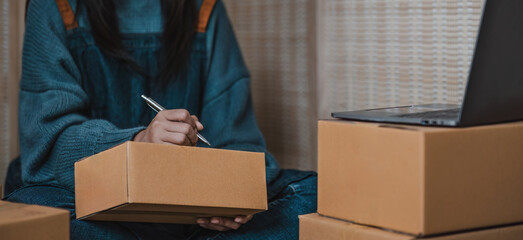 Close-up of business owner hand writing on parcel boxes to deliver products to customers at home.
