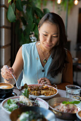 A young Asian woman sits eating pasta at a table in a cafe.