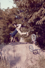Dangerous tricks, falling down. Young man, extreme sport lover riding bmx bicycle, training outdoors on hills in forest. Concept of active lifestyle, sport, extreme, dynamics, hobby, freestyle