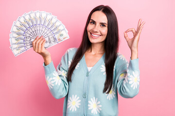 Photo of cheerful positive lady wear flower print cardigan showing okey sign rising cash fan isolated pink color background