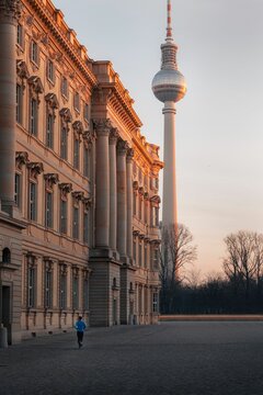 man in blue running on pavement in front of large beige building with tv tower