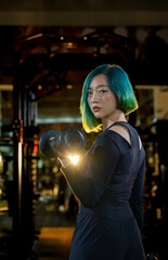 Fototapeta premium fashion hairstyle asian woman lifting dumbbell in one hand energizing strong exercise at modern gym, active fitness people workout functional training for body and mental health in dark sport club